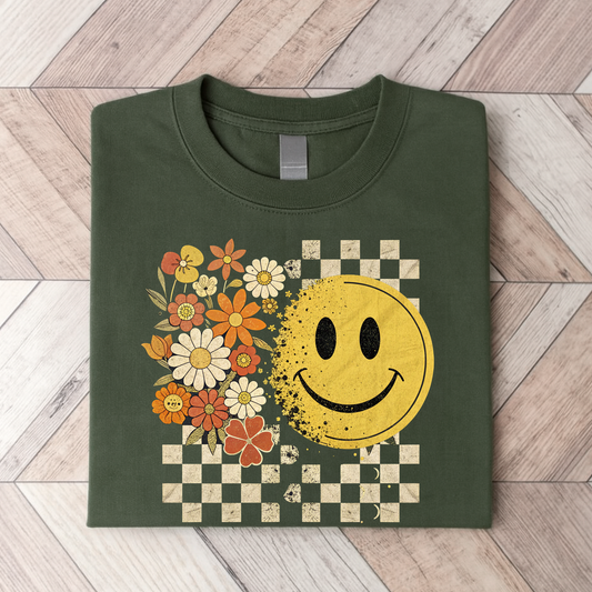Green t-shirt with a smiley face and floral design on a wooden floor.