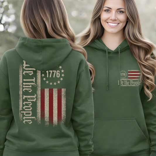 Green hoodie with 'We The People' and 1776 design on front and back worn by a woman outdoors.