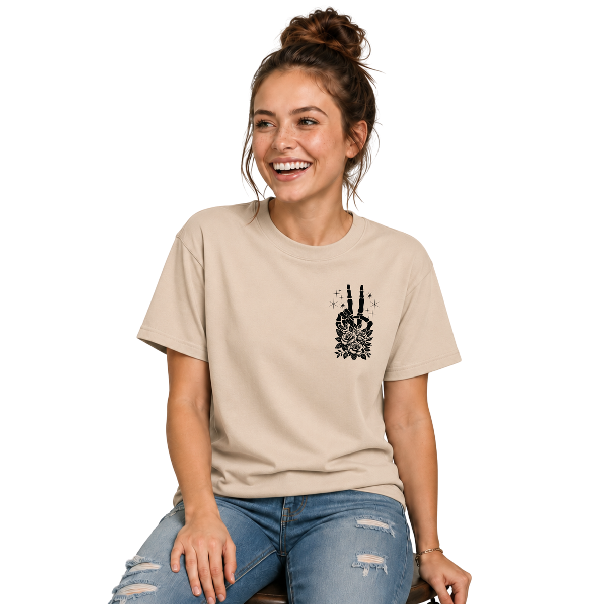 Woman wearing a sand T-shirt with a small black floral skeleton peace-sign graphic on the left chest.