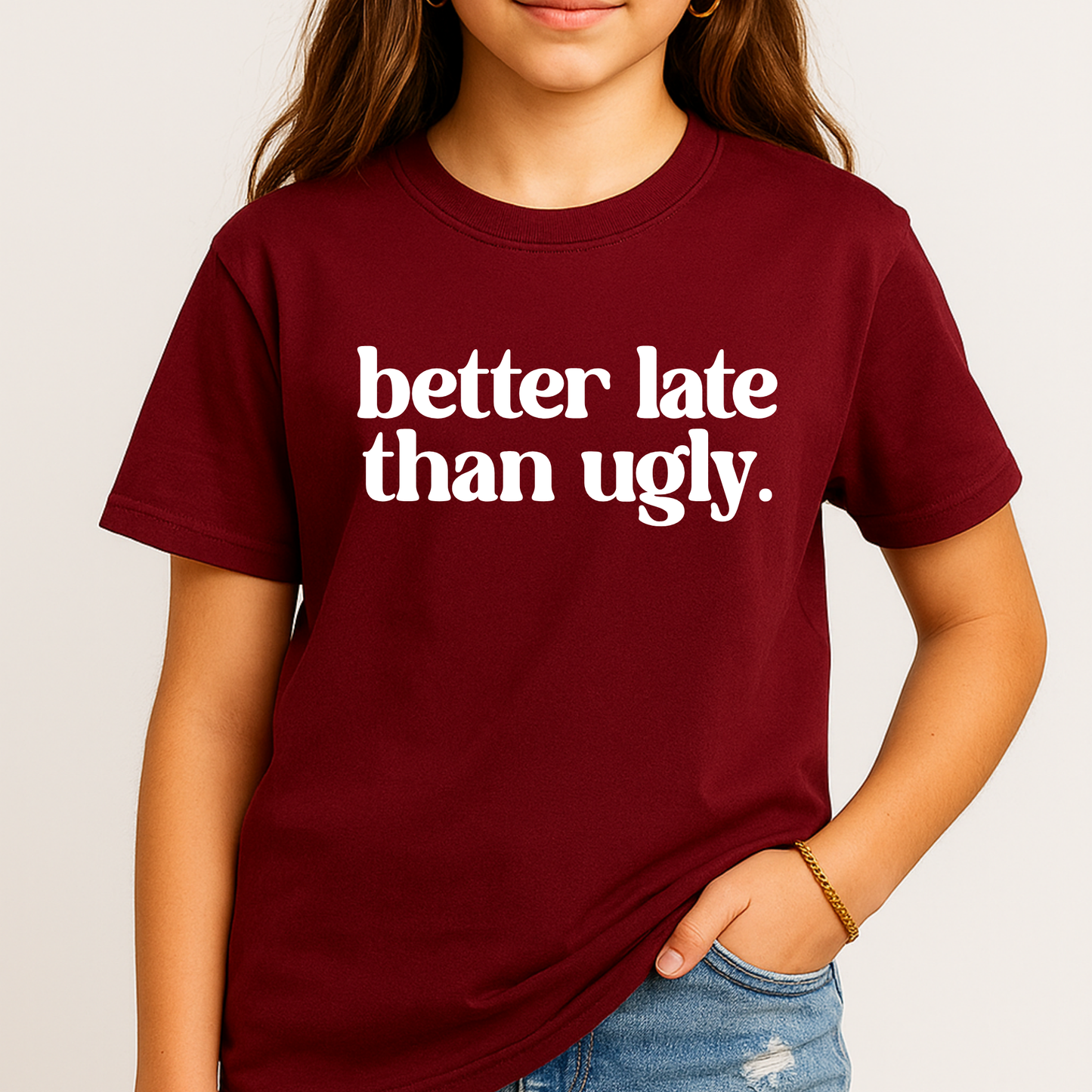 Person wearing a maroon t-shirt with 'better late than ugly' text on a plain background