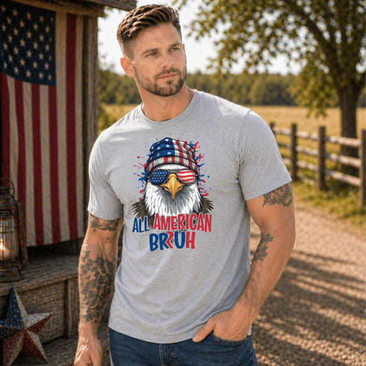 Man wearing a t-shirt with an eagle graphic and text, standing outdoors with American flag and barn in background.