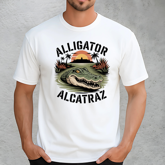 Close-up of a man in a white Alligator Alcatraz shirt with bold swamp and gator print. Features the historic Alcatraz island backdrop and sunset scene. Unisex fit ideal for casual wear, gifts, or tourist apparel.