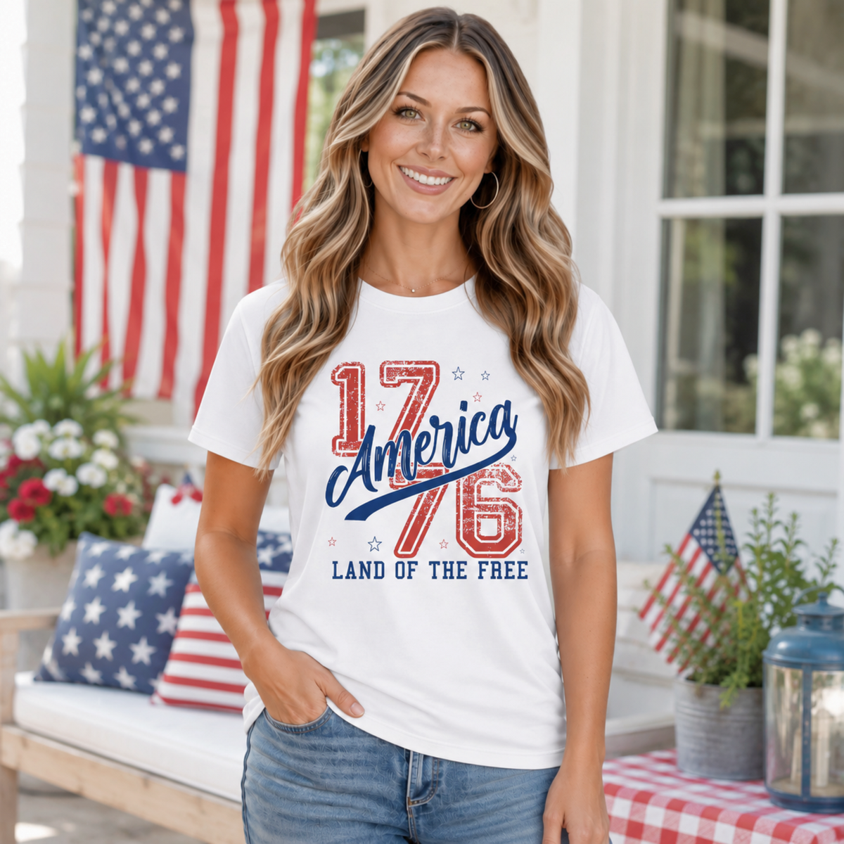 Woman wearing a white America 1776 Land of the Free T-shirt on a patriotic front porch with American flags and red, white, and blue decor