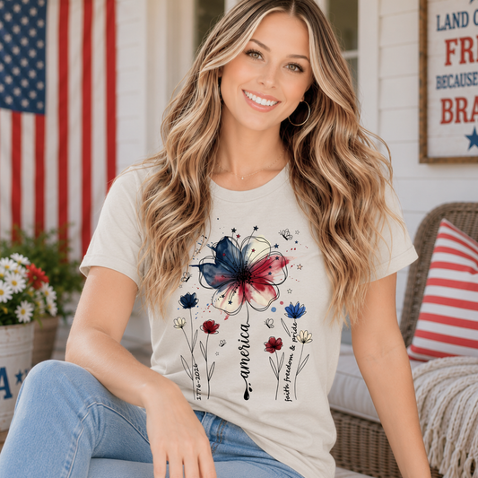 Woman wearing America 250 floral patriotic shirt with watercolor red white and blue flower graphic and Faith Family Freedom artwork