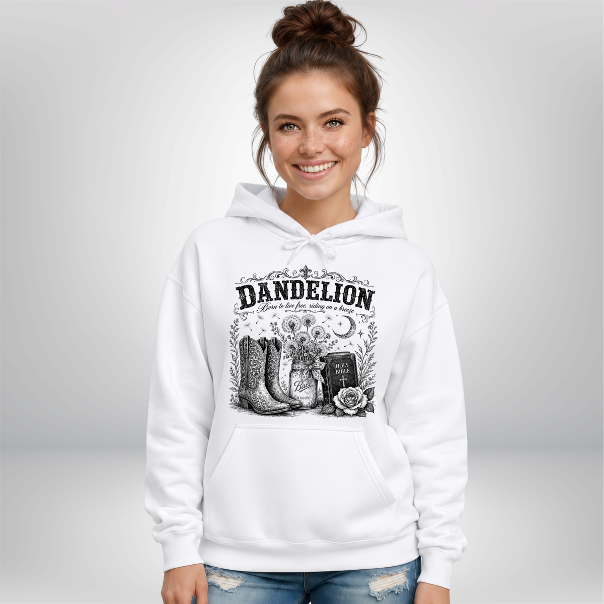 Woman wearing a white Dandelion pullover hoodie with cowboy boots, dandelion-filled mason jar, Holy Bible, rose, and crescent moon graphic on a white background