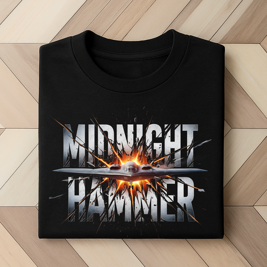 Folded black Midnight Hammer shirt with explosive bomber graphic – flat lay on wood floor
