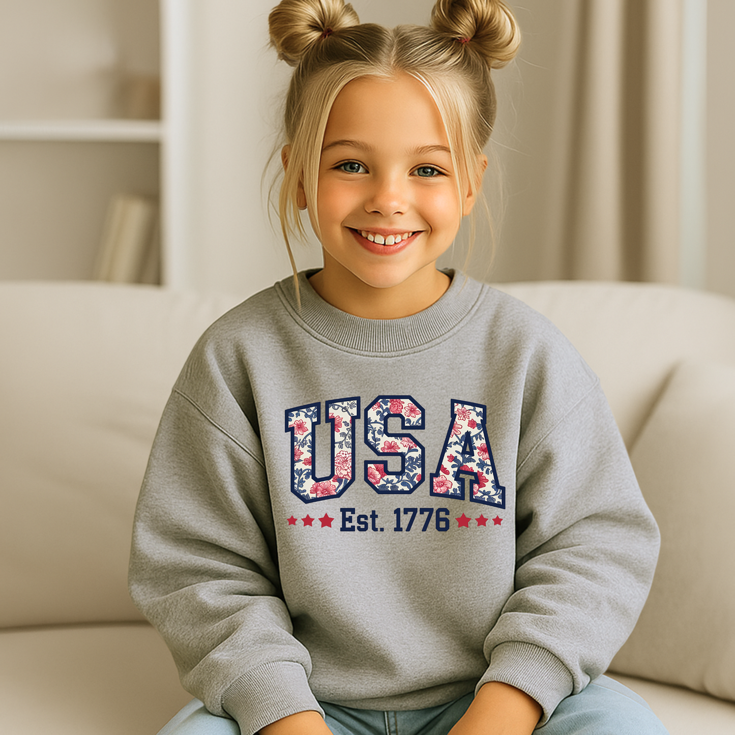 Girl smiling in a gray USA Est. 1776 sweatshirt, cozy indoor setting.