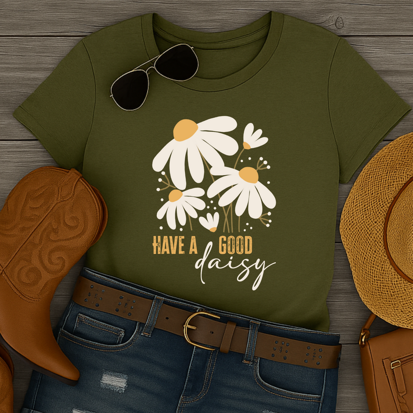 Green Have a Good Daisy t-shirt with daisy design and text, paired with cowboy boot, jeans, and hat on wooden surface