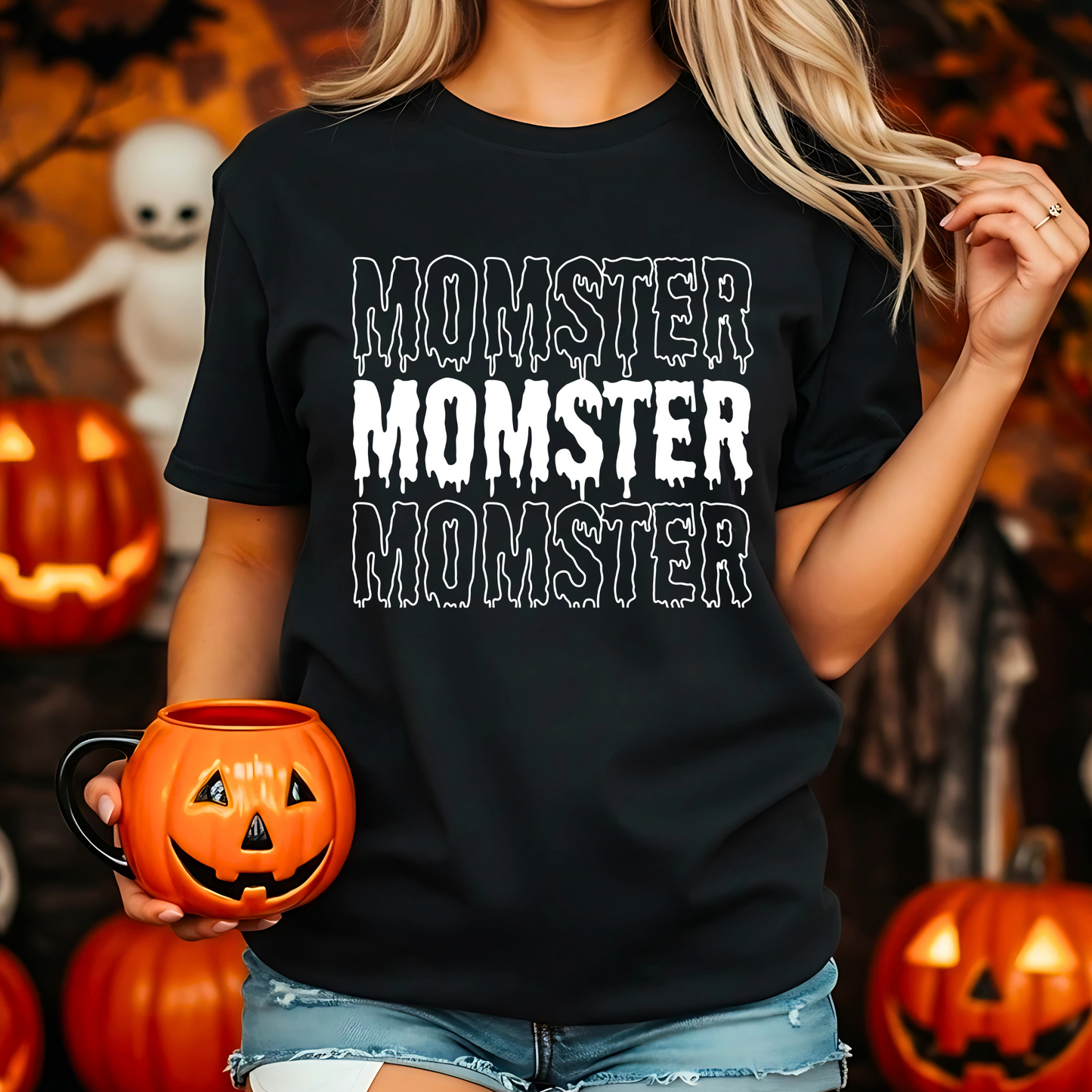 A Mom wearing a black t-shirt with 'MOMSTER' text, holding a pumpkin mug in a Halloween-themed setting.