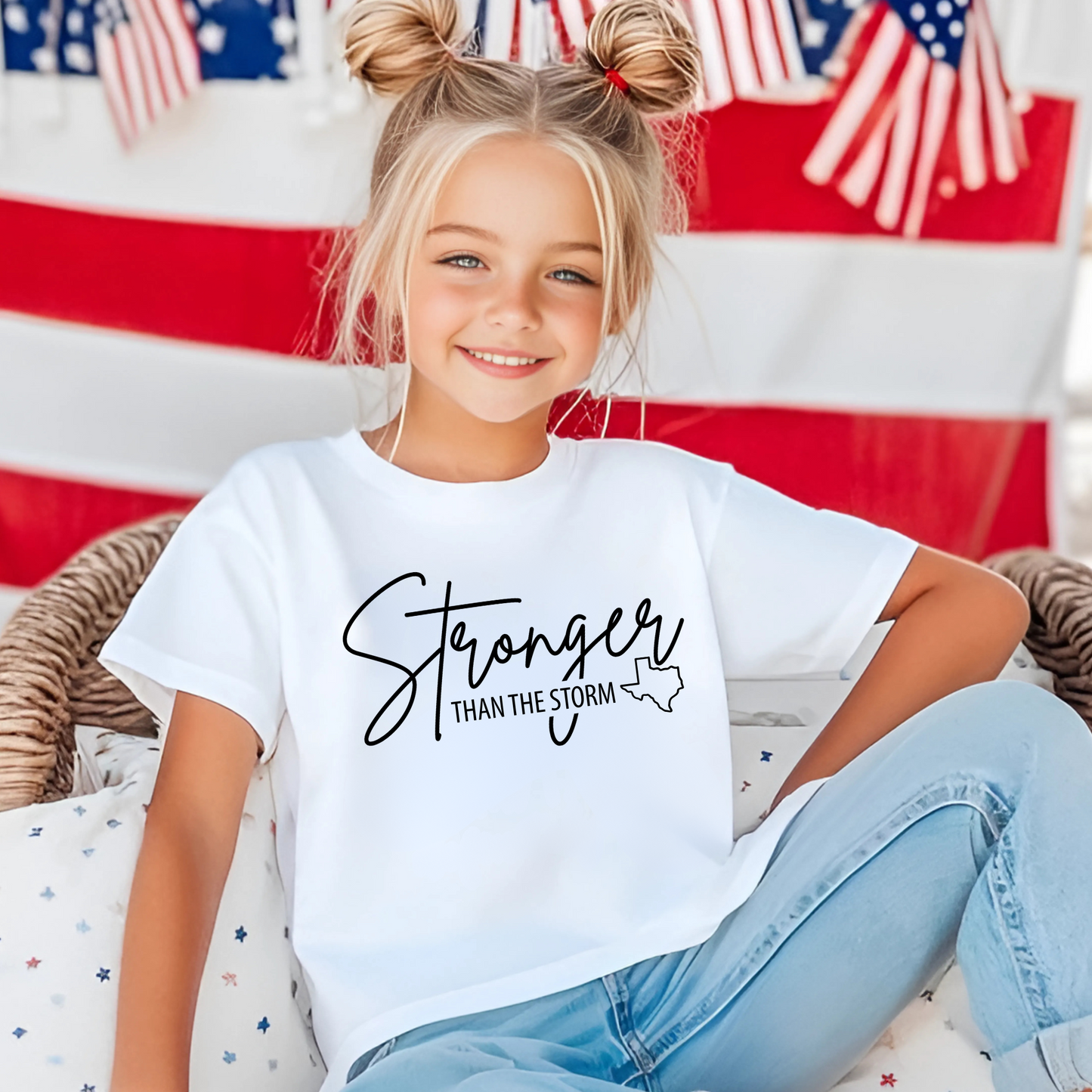 Patriotic kids’ shirt – white “Stronger Than the Storm” Texas tee for girls with USA flag backdrop.
