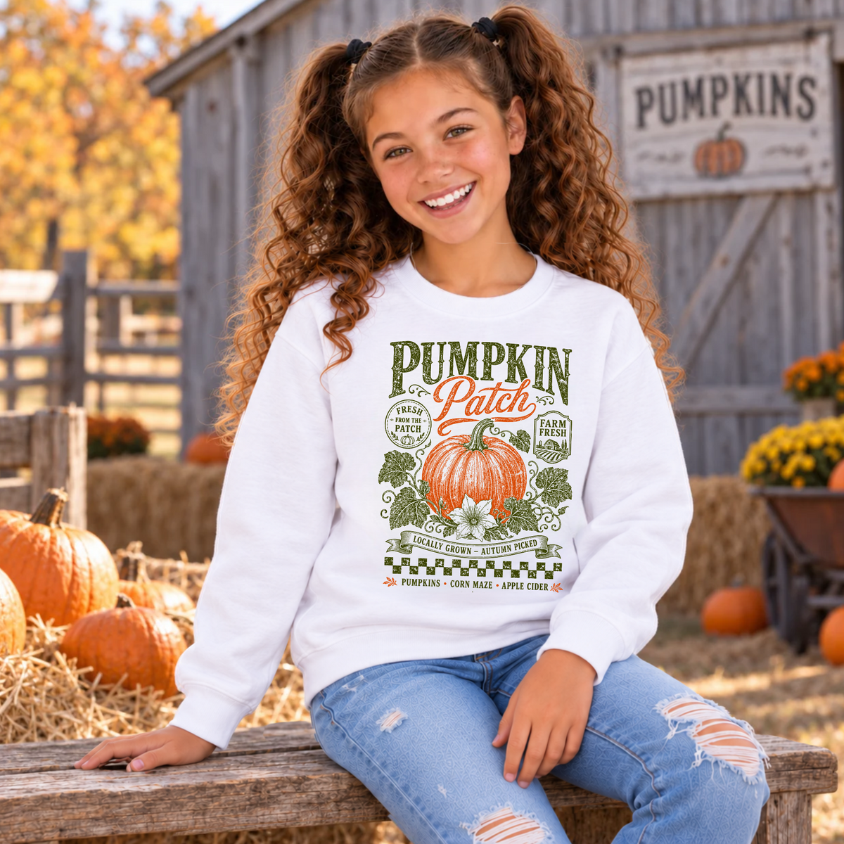Smiling girl in a white youth sweatshirt featuring the vintage Pumpkin Patch pumpkin, floral and farm-market design at an autumn pumpkin patch
