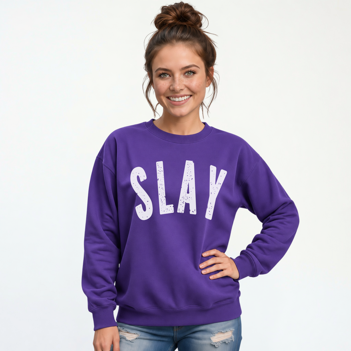 Woman wearing a purple SLAY crewneck sweatshirt with bold white distressed lettering against a white studio background.
