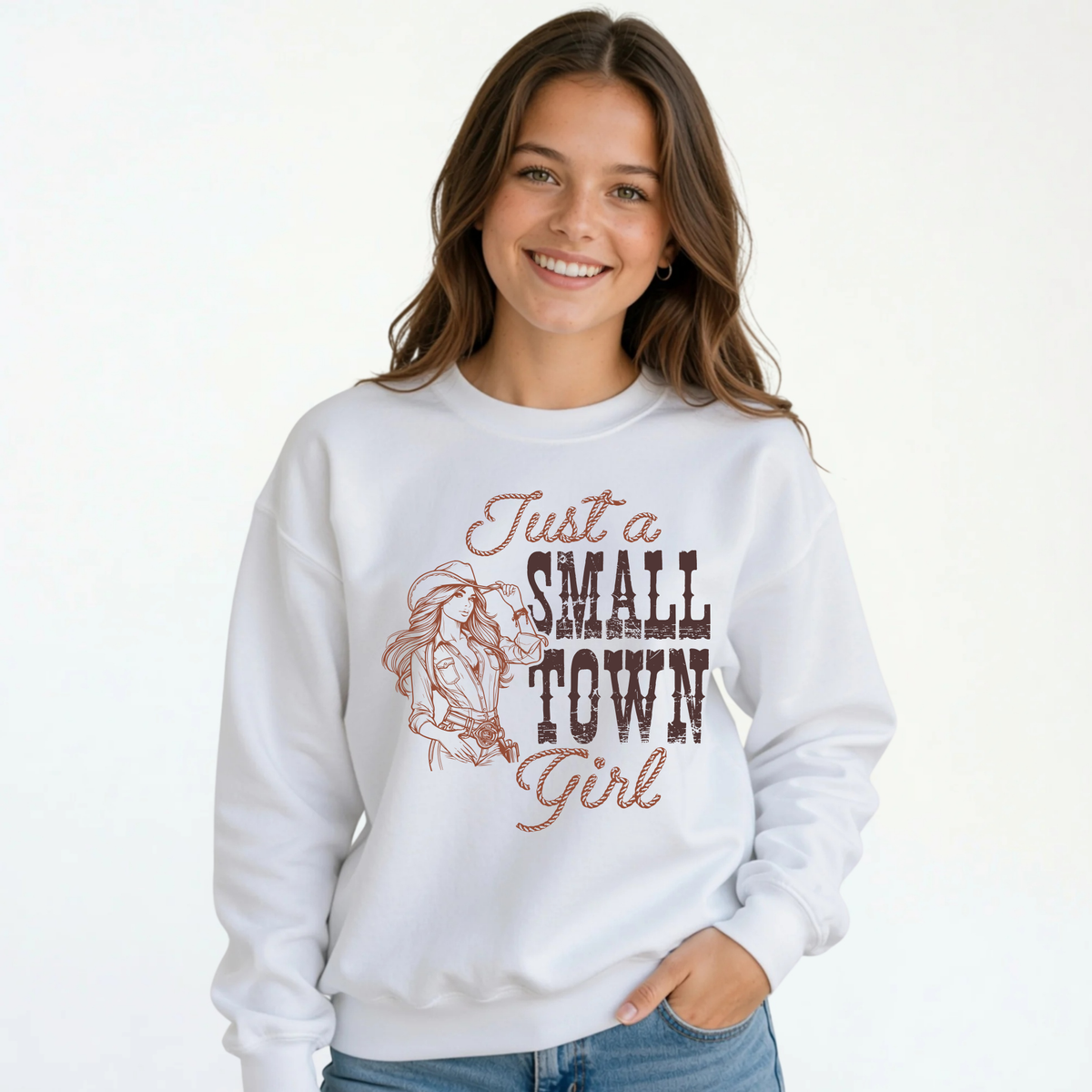Smiling young female model wearing a white youth crewneck sweatshirt with the “Just a Small Town Girl” western cowgirl graphic, paired with blue jeans against a clean white background.