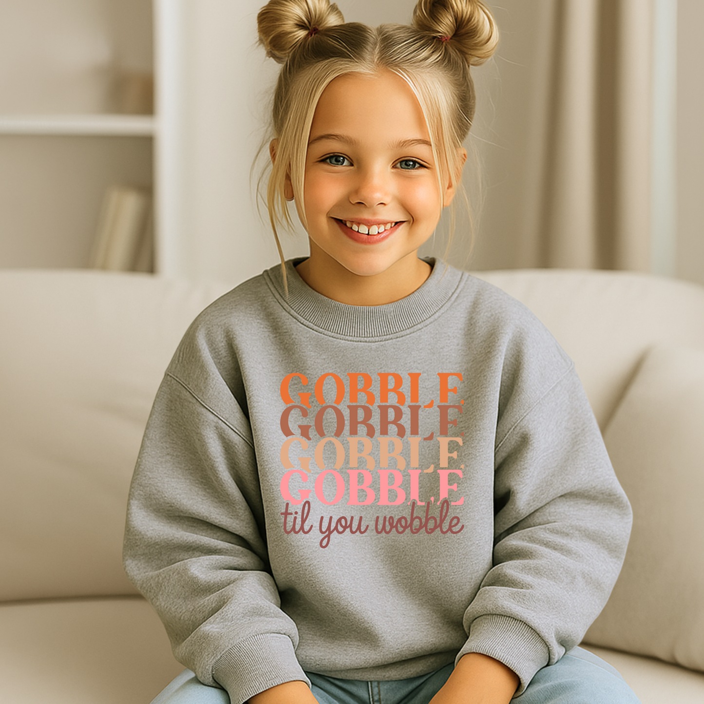 Smiling girl in a sports gray youth sweatshirt featuring the festive phrase "Gobble Til You Wobble" in autumn tones. A comfy unisex pullover for Thanksgiving, fall school events, and holiday celebrations.