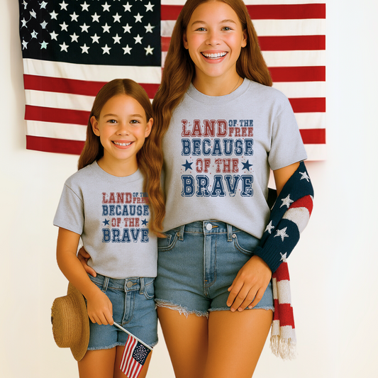 Teen and young girl matching in patriotic "Land of the Free Because of the Brave" t-shirts in front of American flags.
