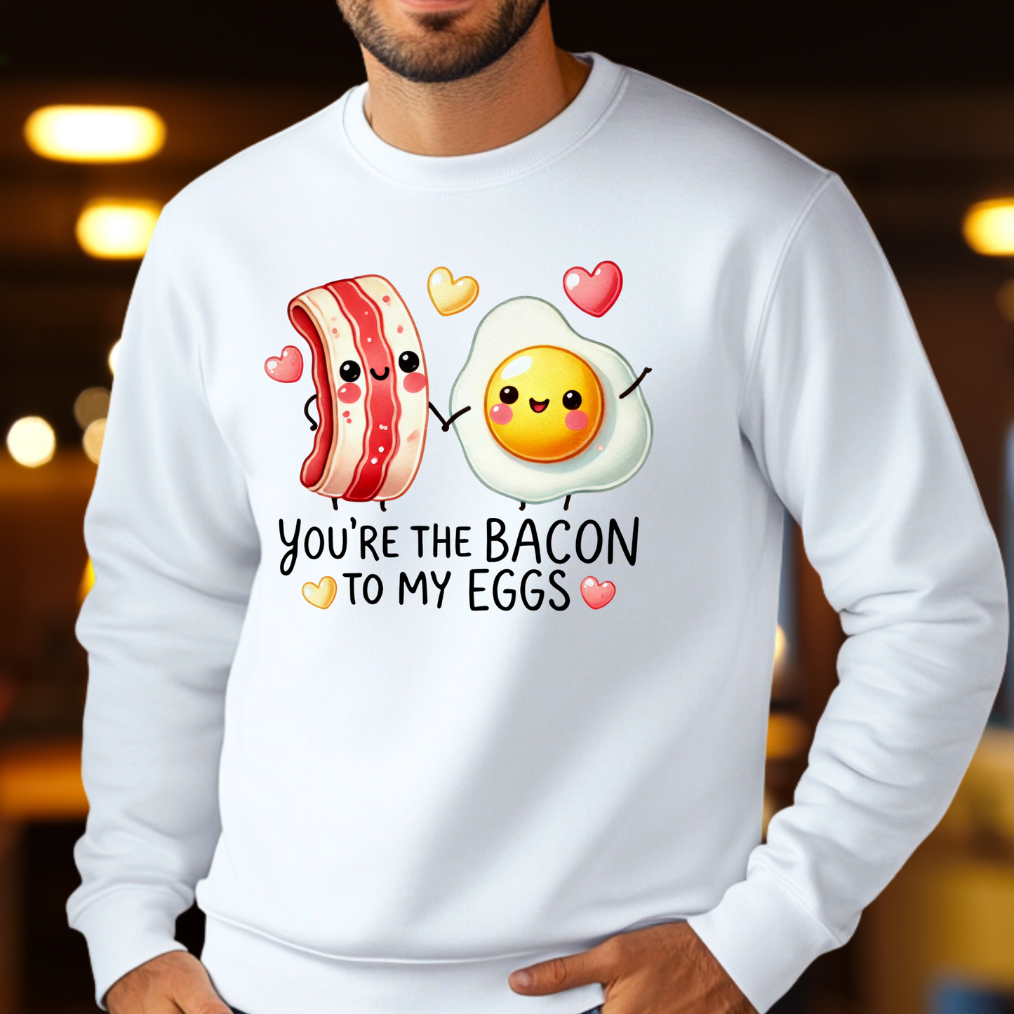 Man in a white sweatshirt with a kawaii-style bacon and egg graphic surrounded by hearts, and the phrase “You're the Bacon to My Eggs.”
