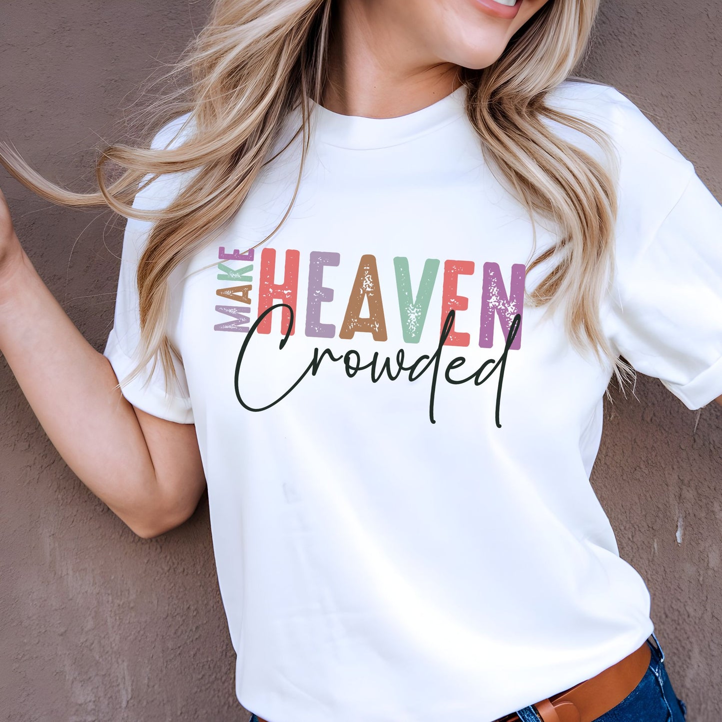 Woman wearing white Make Heaven Crowded graphic T-shirt leaning against wall with hand in hair