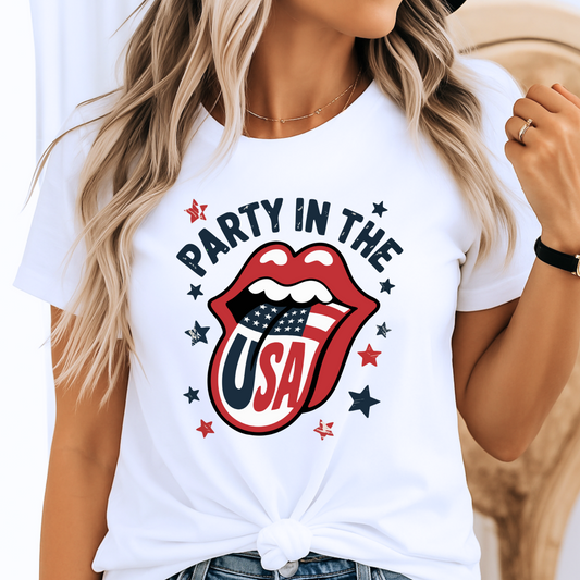 Woman wearing a white “Party in the USA” T-shirt with bold patriotic lips and flag tongue design, styled with a front knot. Perfect for 4th of July BBQs, Memorial Day events, and summer USA pride outfits.
