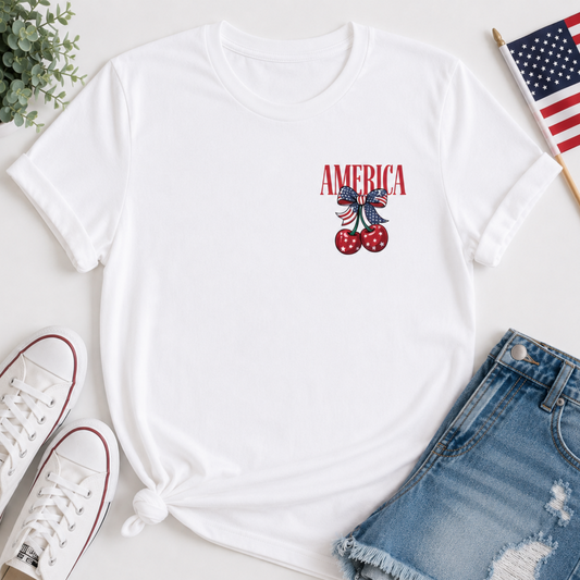 White t-shirt with 'AMERICA' and cherry design, paired with white sneakers and denim shorts on a light surface.