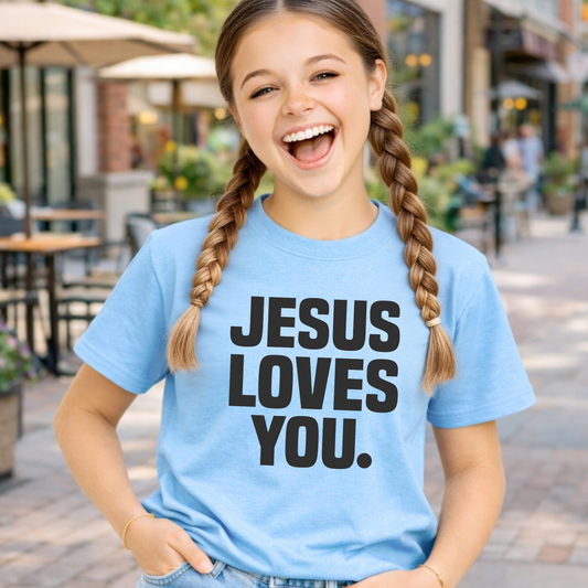 Young girl wearing a blue t-shirt with 'Jesus Loves You' text, standing outdoors.