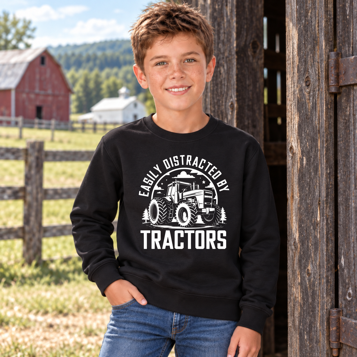 Boy wearing a black youth Easily Distracted by Tractors sweatshirt at a rustic barn doorway.