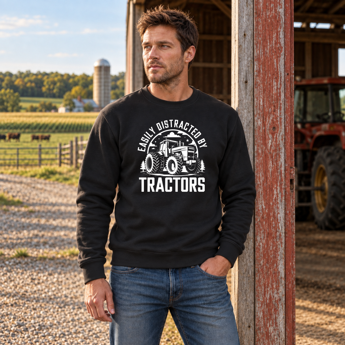 Man wearing a black Easily Distracted by Tractors sweatshirt by a red barn with a tractor inside.