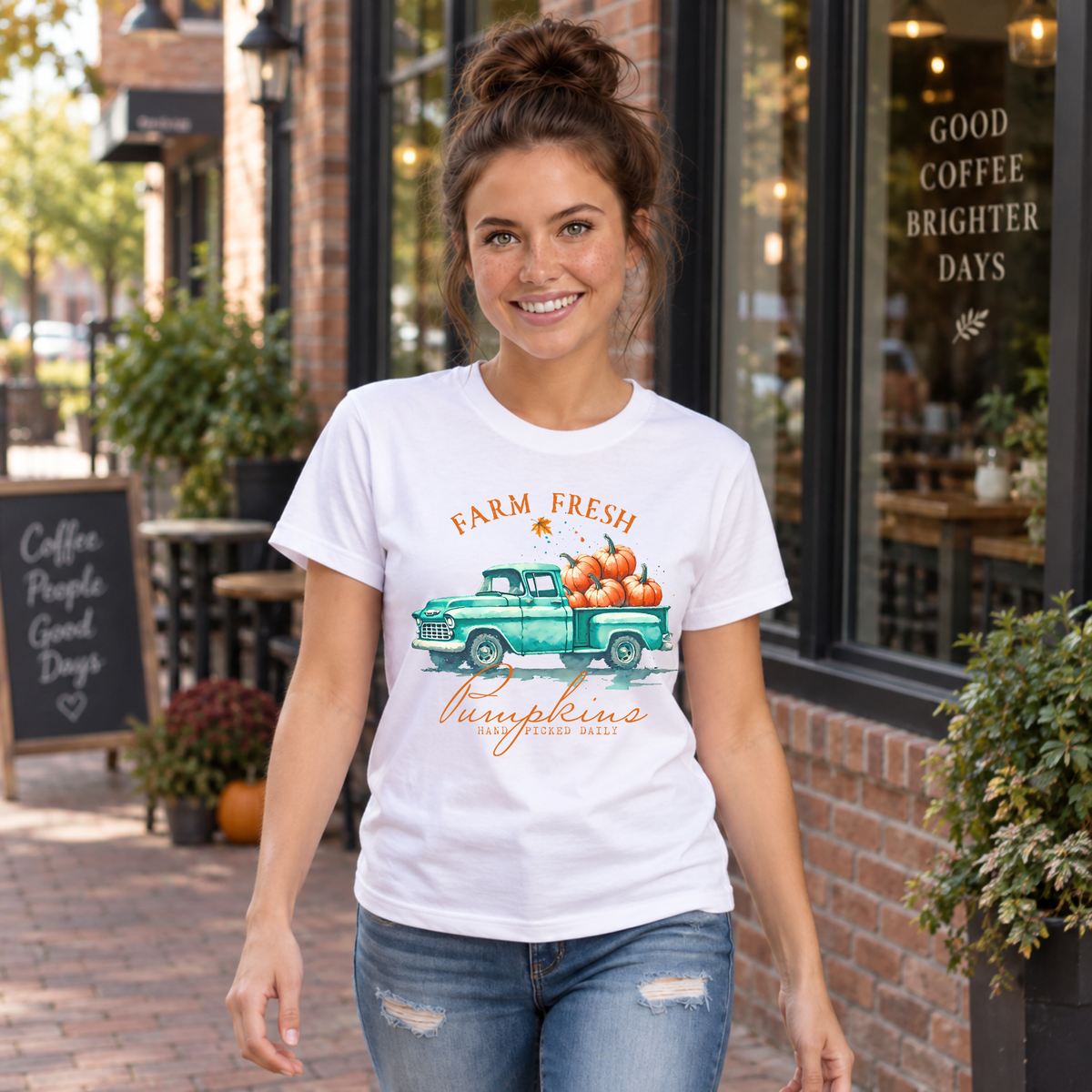 Woman in a white T-shirt with a vintage teal pumpkin truck and Farm Fresh Pumpkins design walking outside a cafe.