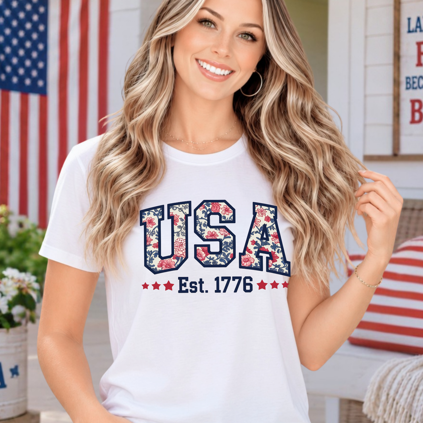 Woman wearing a white t-shirt with 'USA Est. 1776' design in an outdoor setting with American flag and decor.