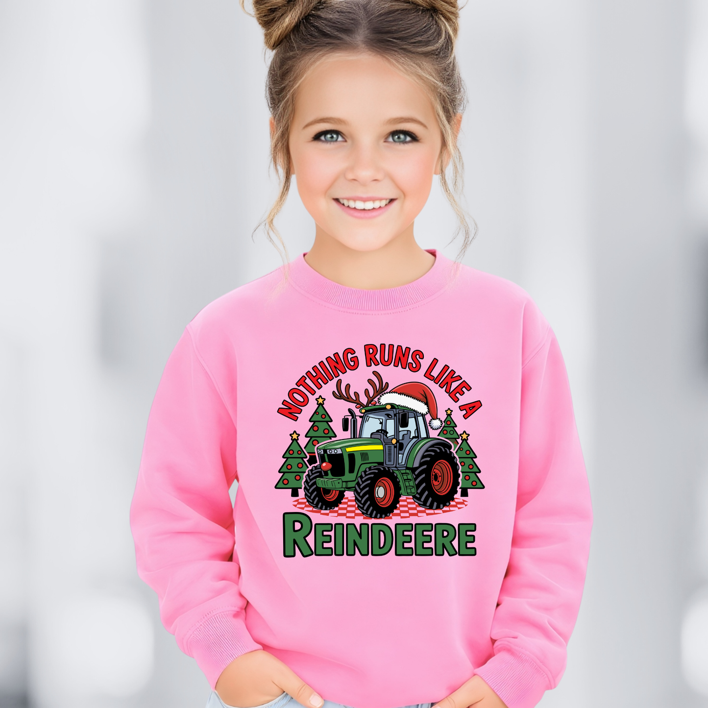 Child wearing a pink sweatshirt with a Christmas-themed tracktor design on a light gray background