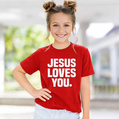 Young girl wearing a red t-shirt with 'Jesus Loves You' text, standing outdoors.