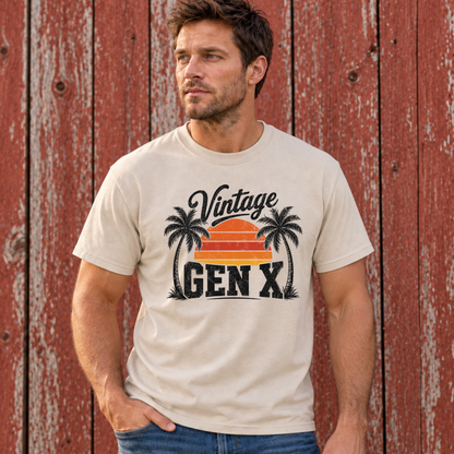 Man wearing a sand Vintage Gen X T-shirt with black palm trees and a striped orange sunset in front of a red barn wall.