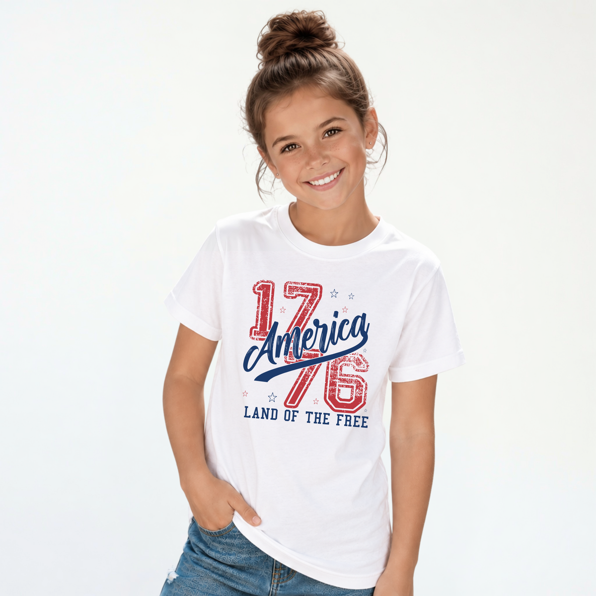 Smiling girl wearing a white youth T-shirt with a distressed red and blue America 1776 Land of the Free graphic