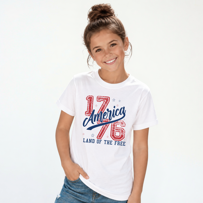 Smiling girl wearing a white youth T-shirt with a distressed red and blue America 1776 Land of the Free graphic