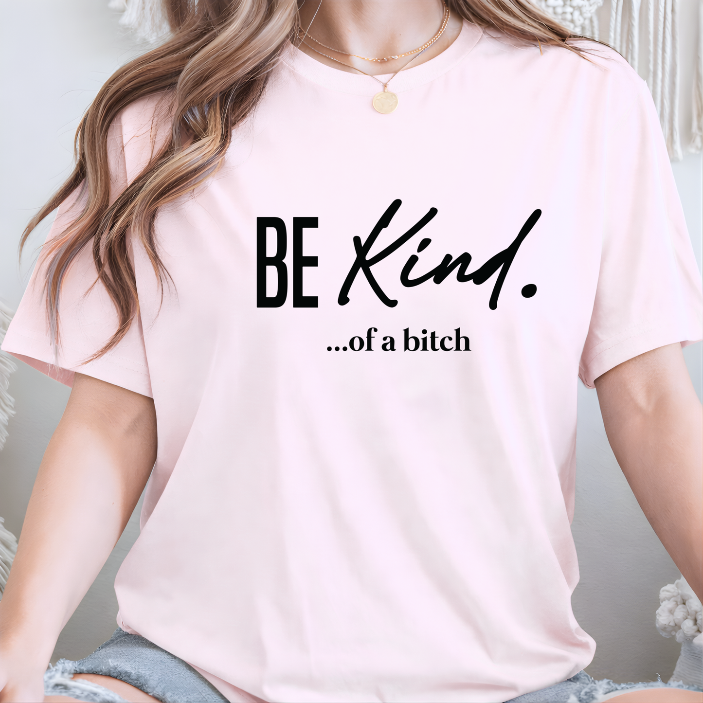 Woman wearing a pink t-shirt with 'BE KIND...of a bitch' text.