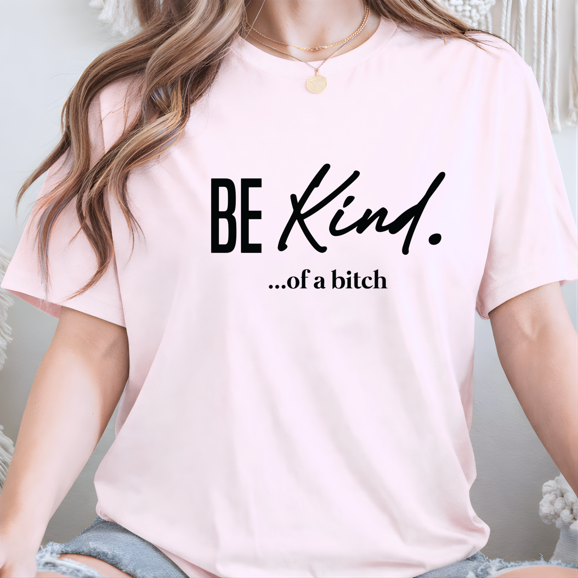 Woman wearing a pink t-shirt with 'BE KIND...of a bitch' text.