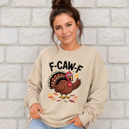 Woman wearing a sand crewneck sweatshirt with a colorful F-CAW-F turkey graphic against a light stone wall.
