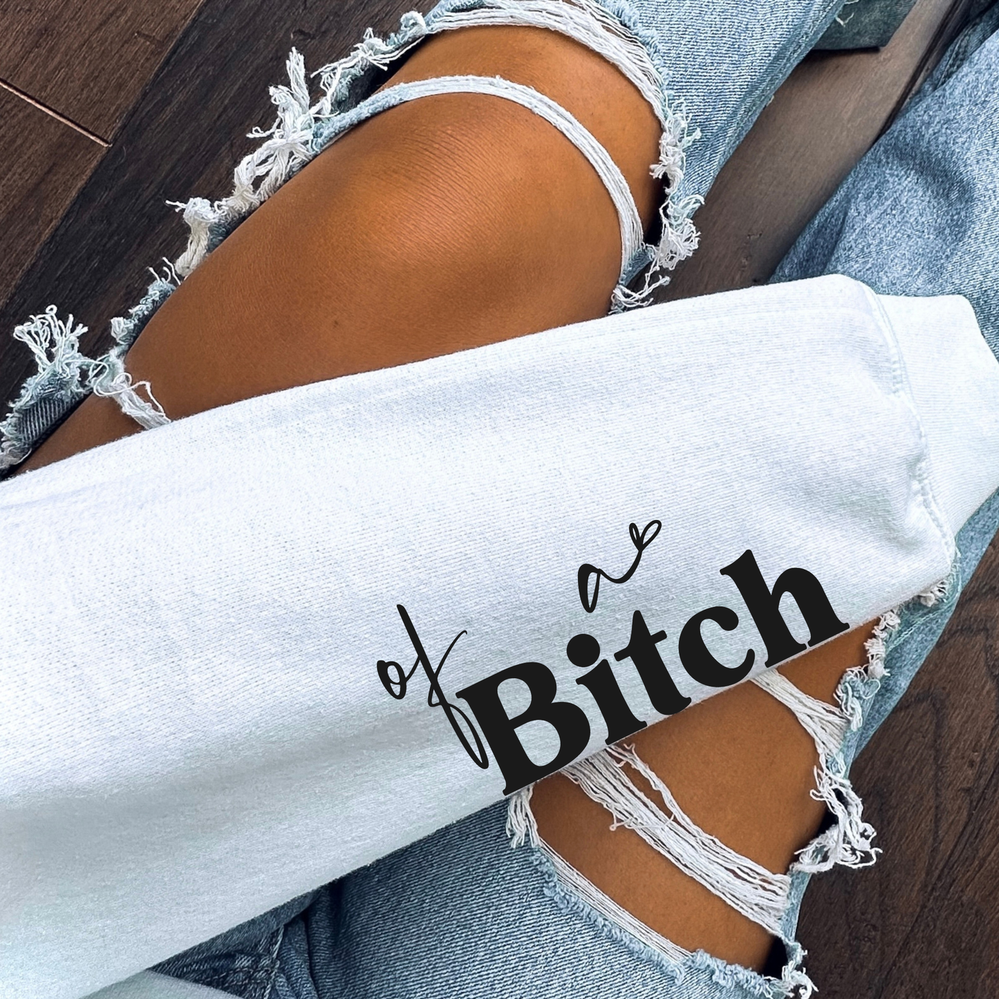 White sweatshirt with text and ripped jeans on a wooden floor.