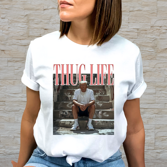 A person wearing a white crew neck t-shirt with a graphic print of a man sitting on steps and the text 'THUG LIFE' above the image.