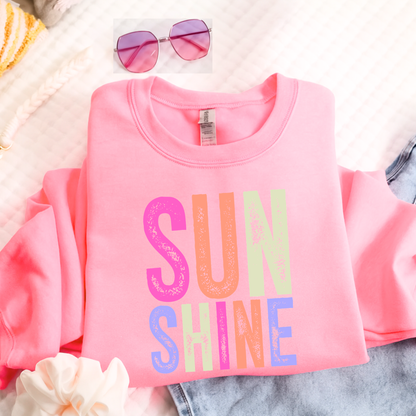 Pink t-shirt with 'SUNSHINE' in colorful letters on a soft surface.