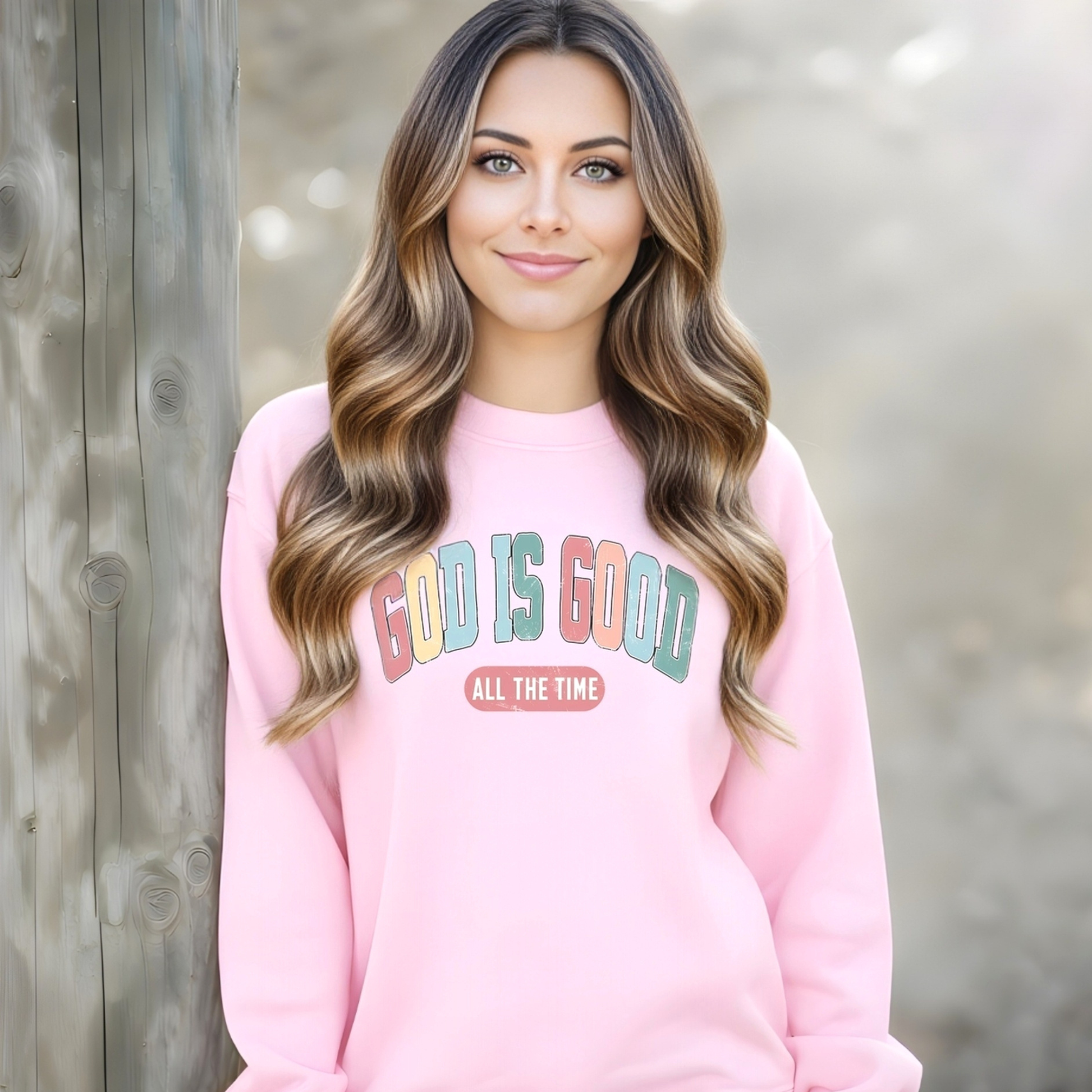 Woman wearing a pink sweatshirt with 'God is Good All the Time' text against a wooden background