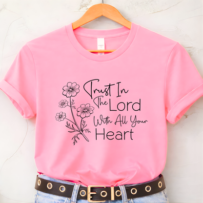 Pink t-shirt with 'Trust In The Lord With All Your Heart' text and floral design on a hanger.