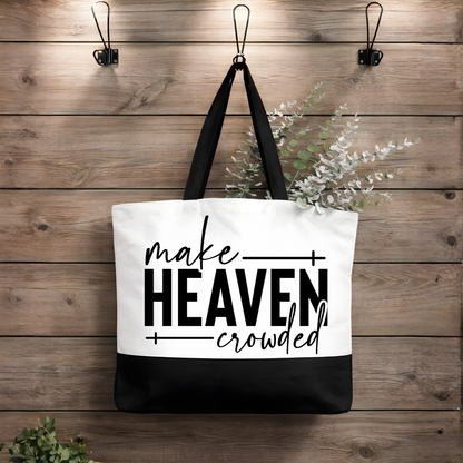 Black and white faith tote bag hanging on wooden wall featuring Make Heaven Crowded Christian design with black straps