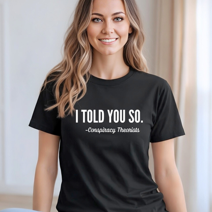 Woman wearing a black t-shirt with "I TOLD YOU SO, Conspirracy Theorist"  text, sitting indoors.
