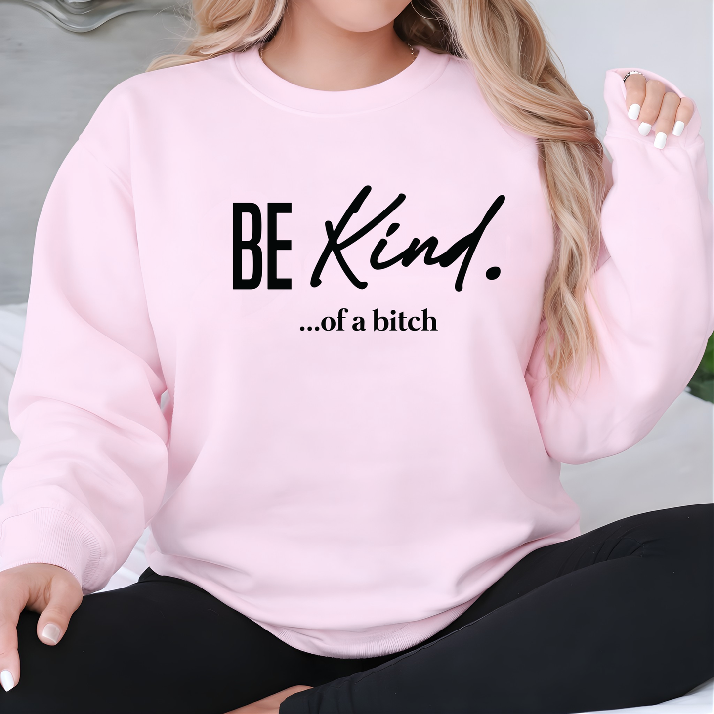 Woman wearing a pink sweatshirt with 'BE KIND. ...of a bitch' text.
