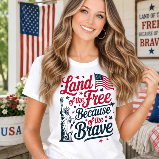 Woman wearing a 'Land of the Free Because of the Brave' t-shirt on a porch with American flags and decor.