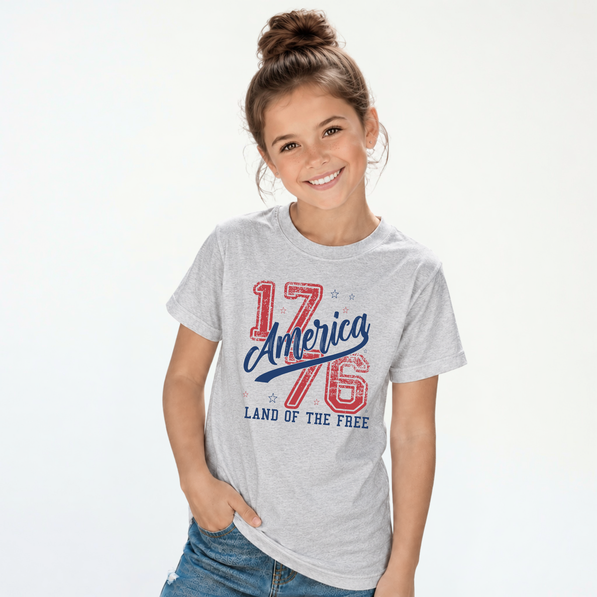 Smiling girl wearing a sports gray youth T-shirt with a distressed red and blue America 1776 Land of the Free graphic