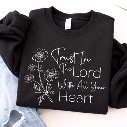 Black sweatshirt with white floral design and text 'Trust In The Lord With All Your Heart' on a light background.