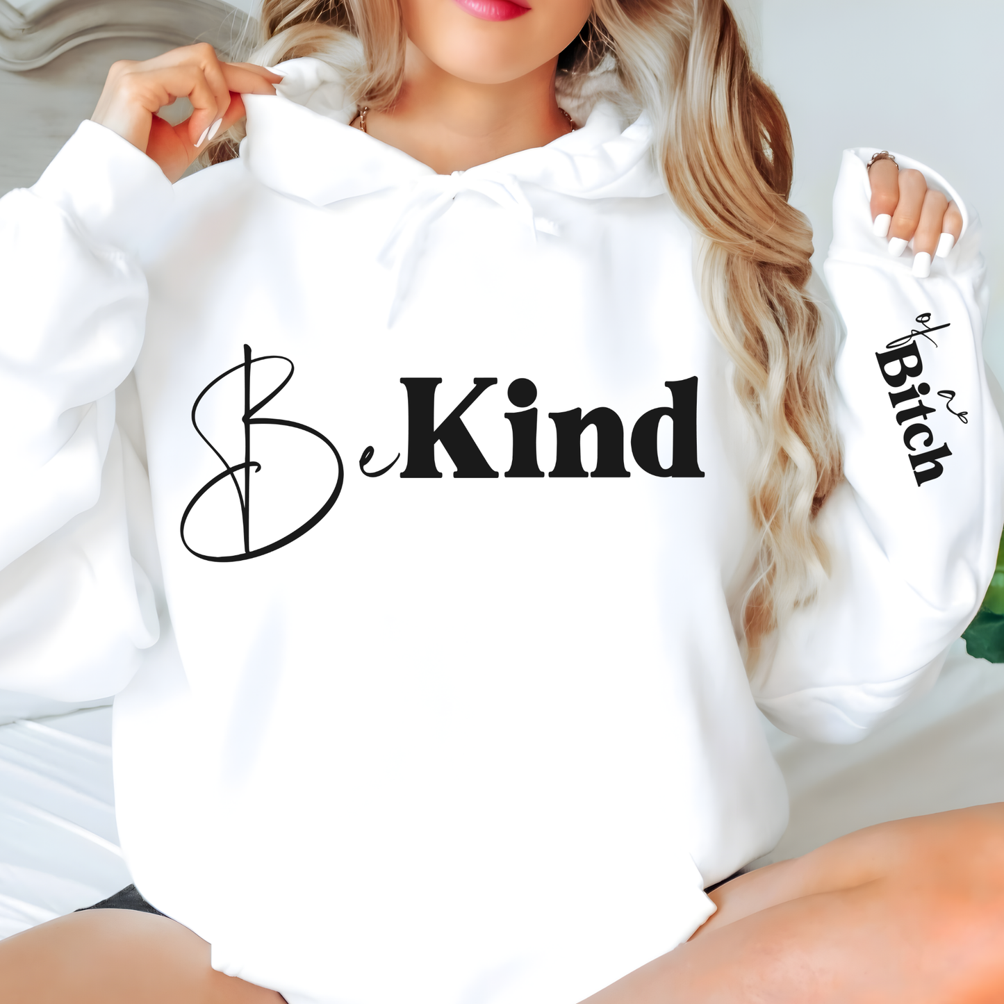 White hoodie with 'Be Kind' text on a blurred background