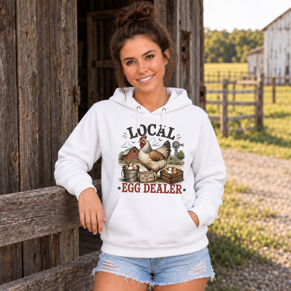Woman in a white Local Egg Dealer hoodie leaning on a rustic farm fence.