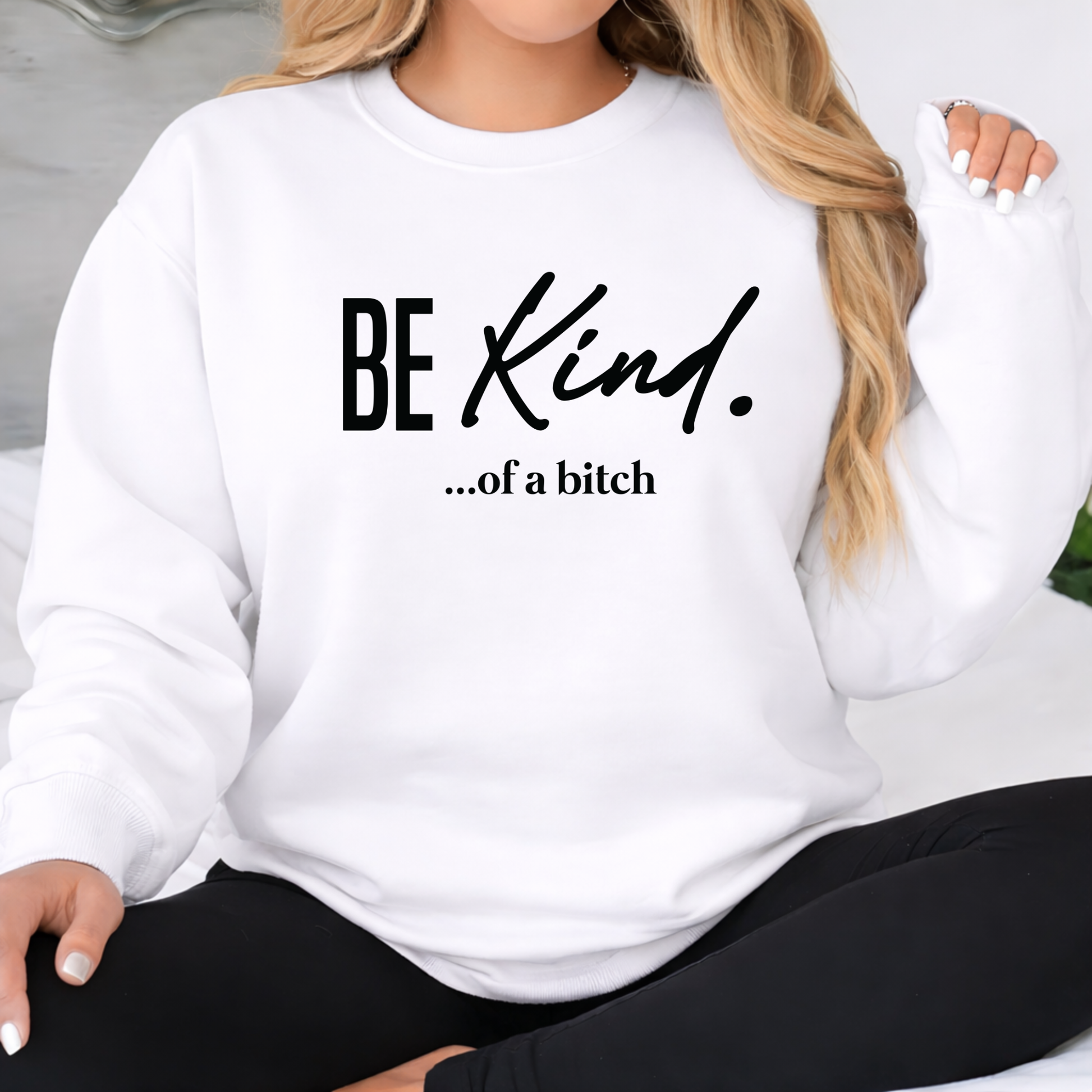 White sweatshirt with 'BE KIND...of a bitch' text worn by a person.